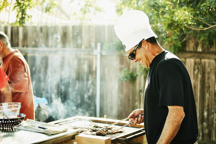 Smiling father wearing a white chef's hat grilling in backyard during family barbecue