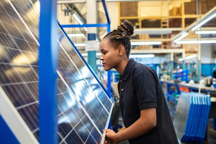Side view of a female employee inspecting newly manufactured solar panels in company. Woman quality engineer examining solar panels in factory.