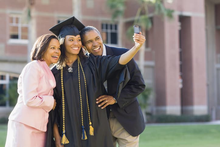 Young female graduate taking photo of parents with smart phone