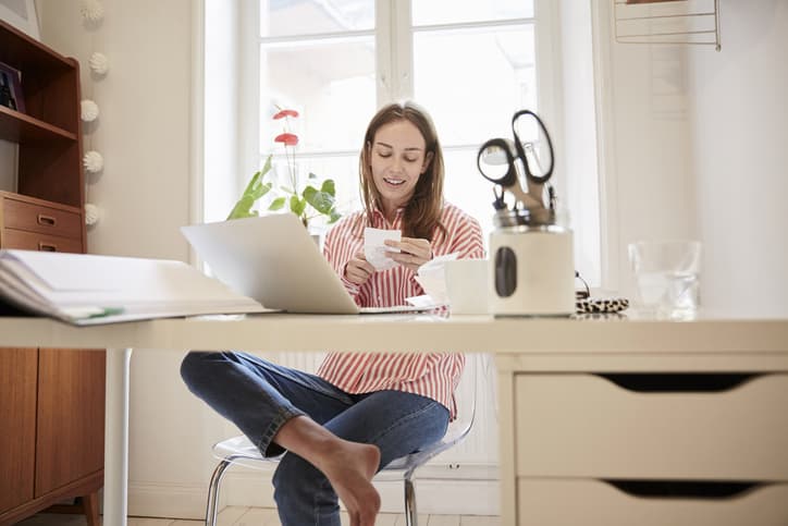 Young woman examining financial bill while working from home while having a drink