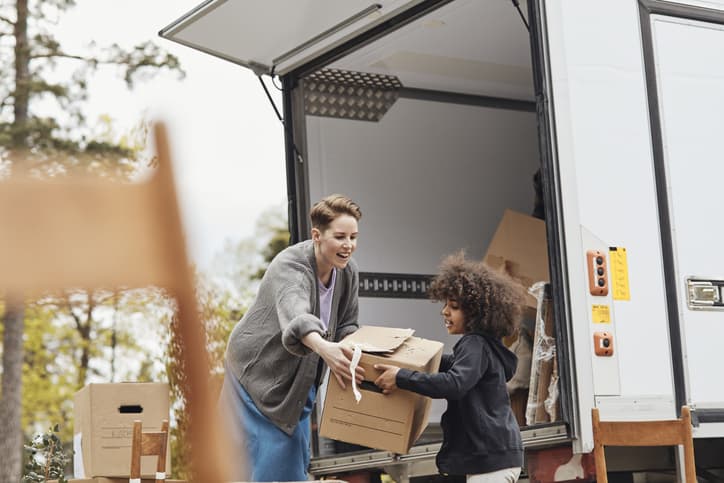 Image of a young boy helping his mother in unloading cardboard boxes from the van