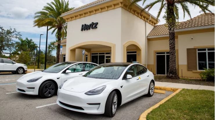 Two electric vehicles parked in front of a Hertz car rental location